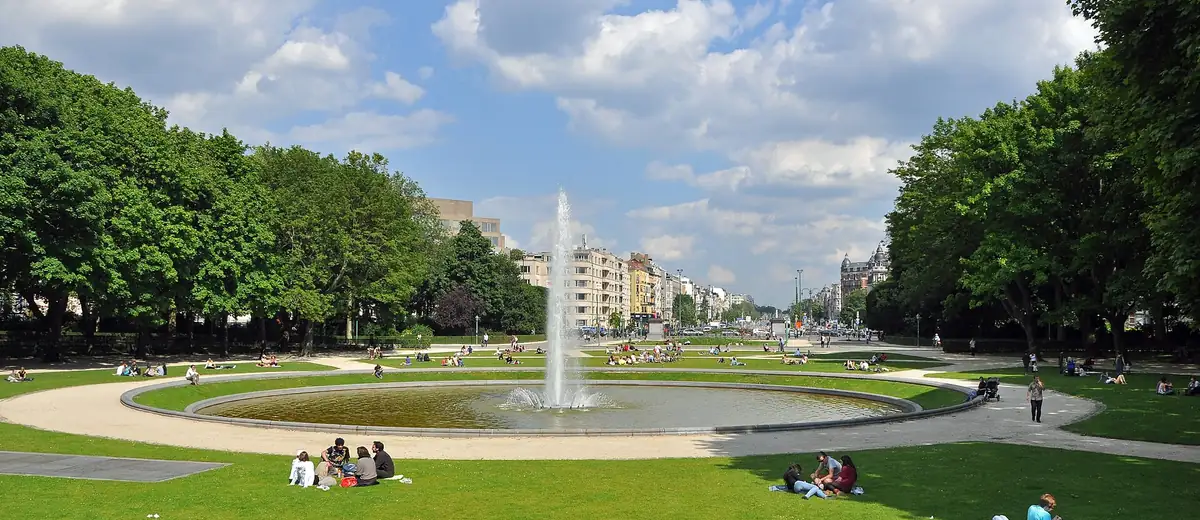 People relaxing on sunny lawns around a fountain in Brussels' Cinquantenaire park