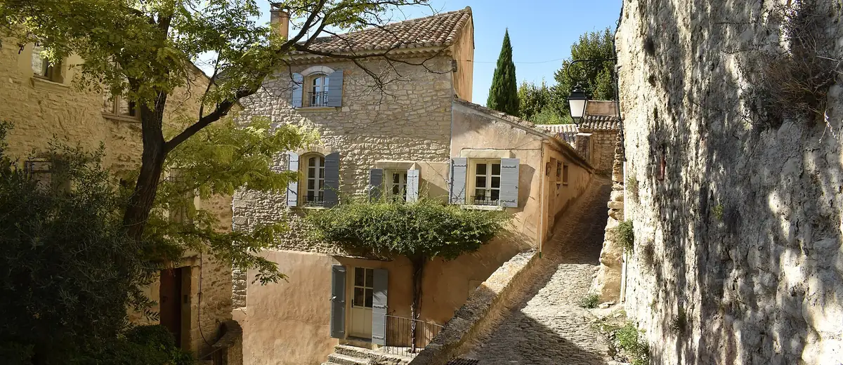 Sunlit cobbled lane with honey-coloured stone houses and blue shutters in Gordes, Provence