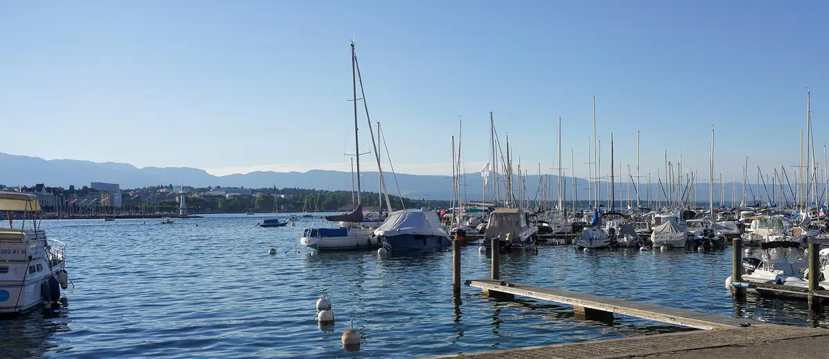 Sailing boats moored in a calm Geneva harbour on a clear summer evening