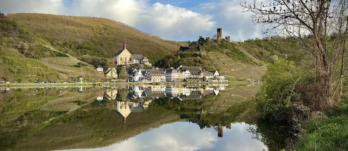 The village of Beilstein mirrored in the still Moselle river between green vineyard hills
