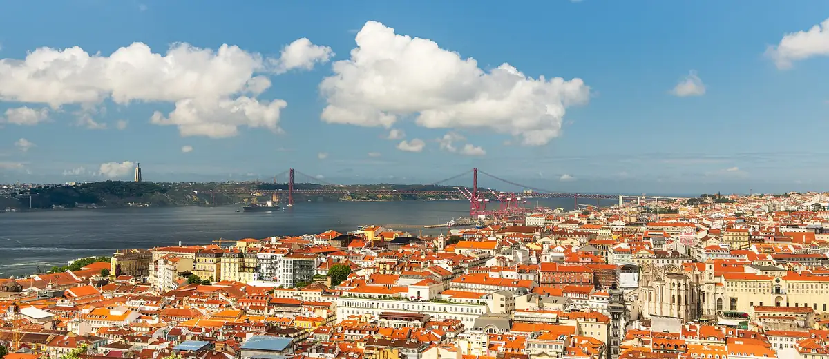 Terracotta rooftops of Lisbon stretching down to the wide Tagus river under soft clouds