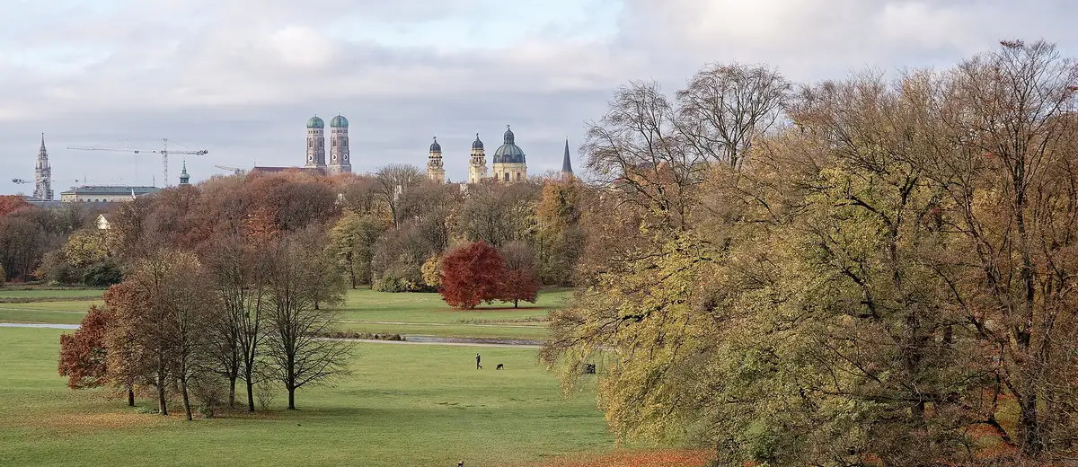 Autumn trees and open meadows of the English Garden, with Munich's old-town towers beyond