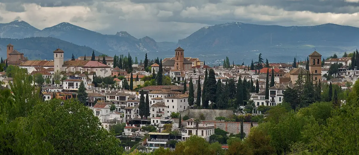Whitewashed houses and cypress trees of Granada's Albaicín against distant blue mountains