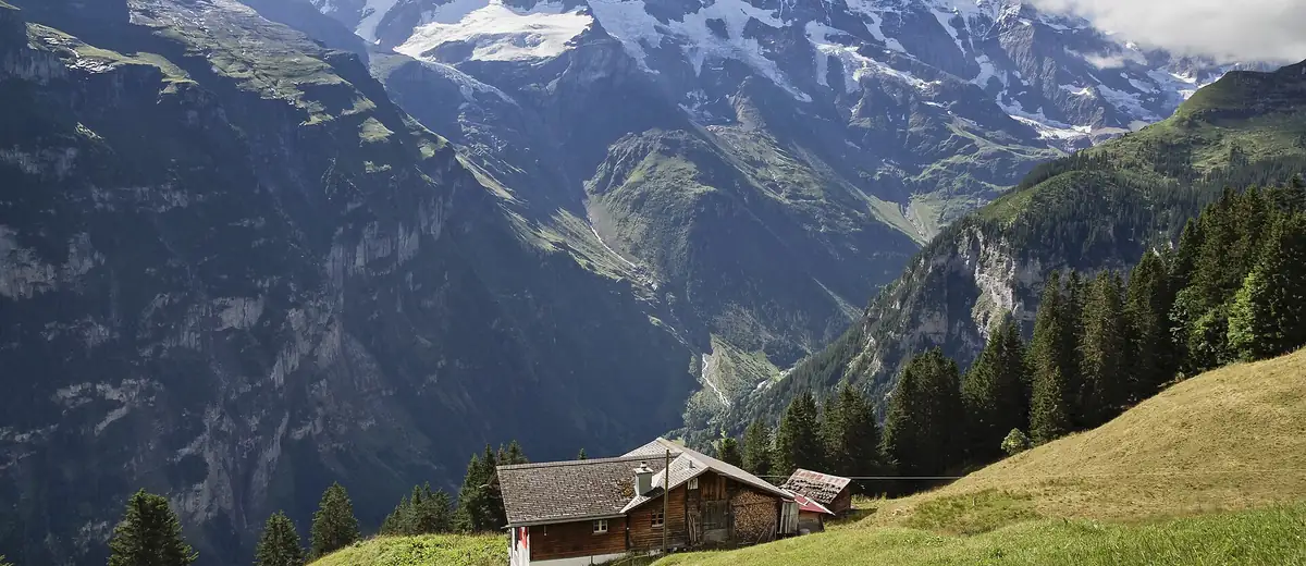 Wooden chalet on a green alpine meadow facing snowy peaks above the Lauterbrunnen valley